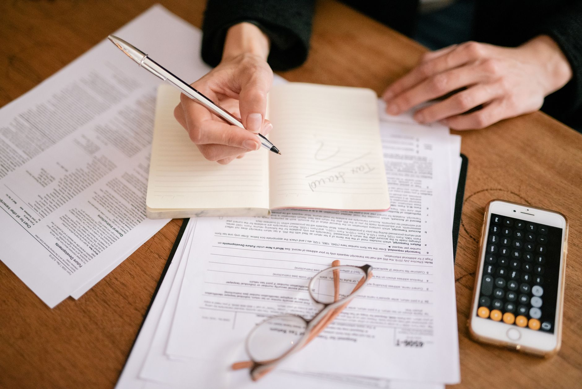 Person writing in notebook with tax forms, glasses and calculator, illustrating HMRC Self Assessment changes for sole traders