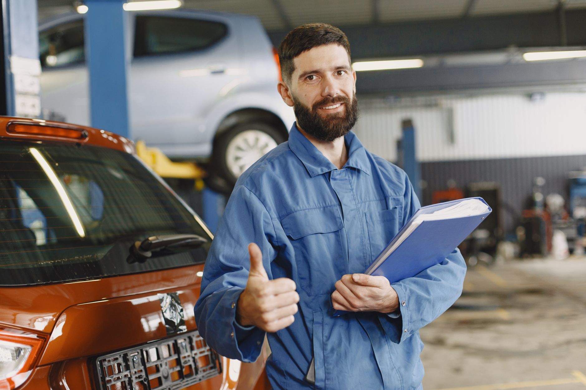 Smiling mechanic giving thumbs up in a garage workshop, illustrating SERMI approval for servicing secure cars