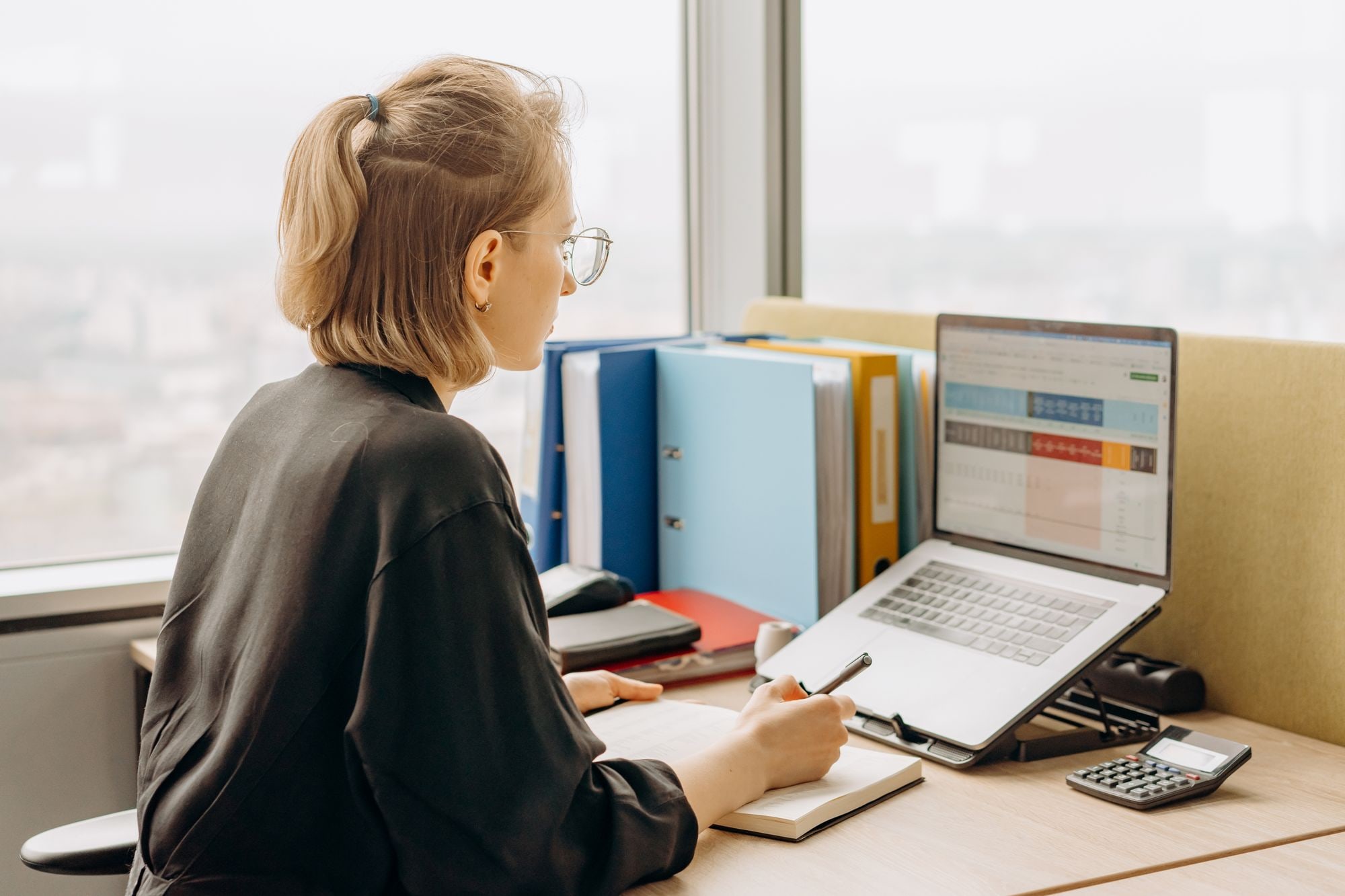 Woman doing cash flow forecasting for small business on a laptop spreadsheet with calculator and files