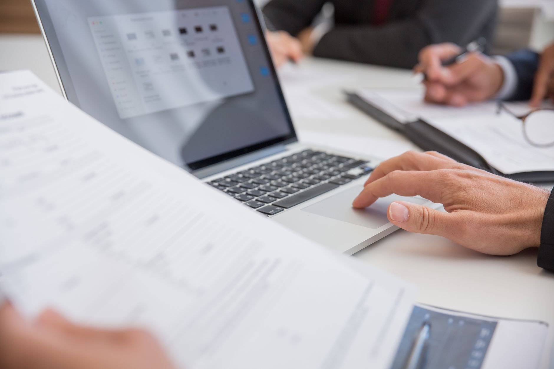 Business professionals reviewing trade and investment factsheets and documents on a laptop in a meeting