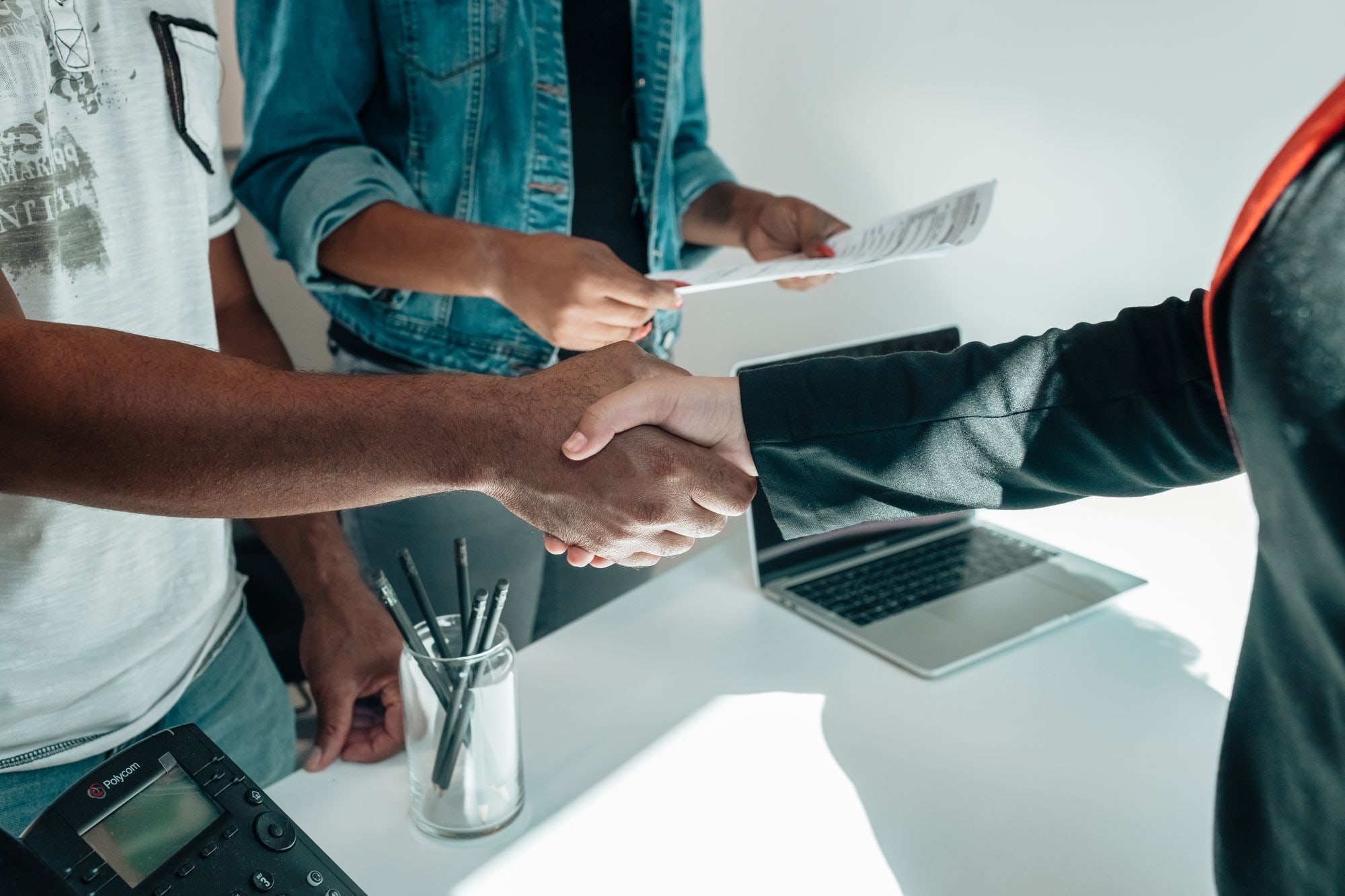 Business people shaking hands over documents and laptop, illustrating how to buy a small business UK