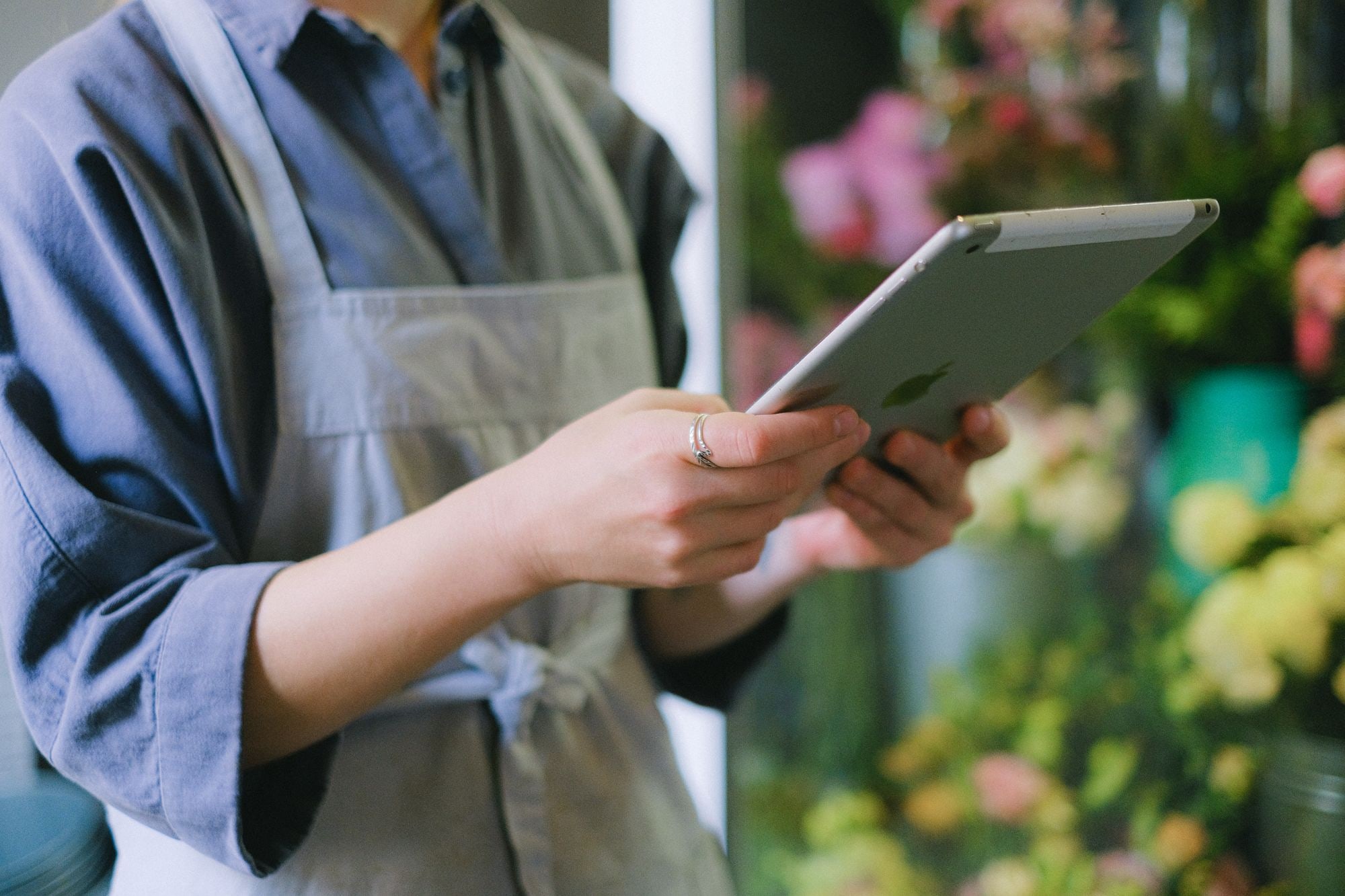 Florist shop worker in apron using a tablet among fresh flowers, illustrating small businesses adopting technology