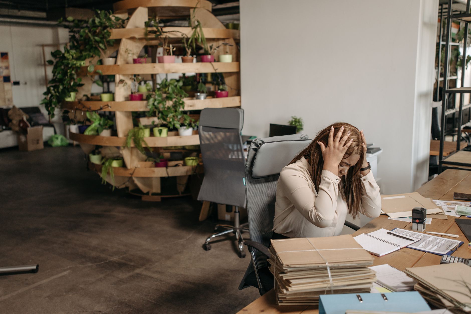 Stressed small business owner holding her head at a desk piled with paperwork, illustrating late payment pressures