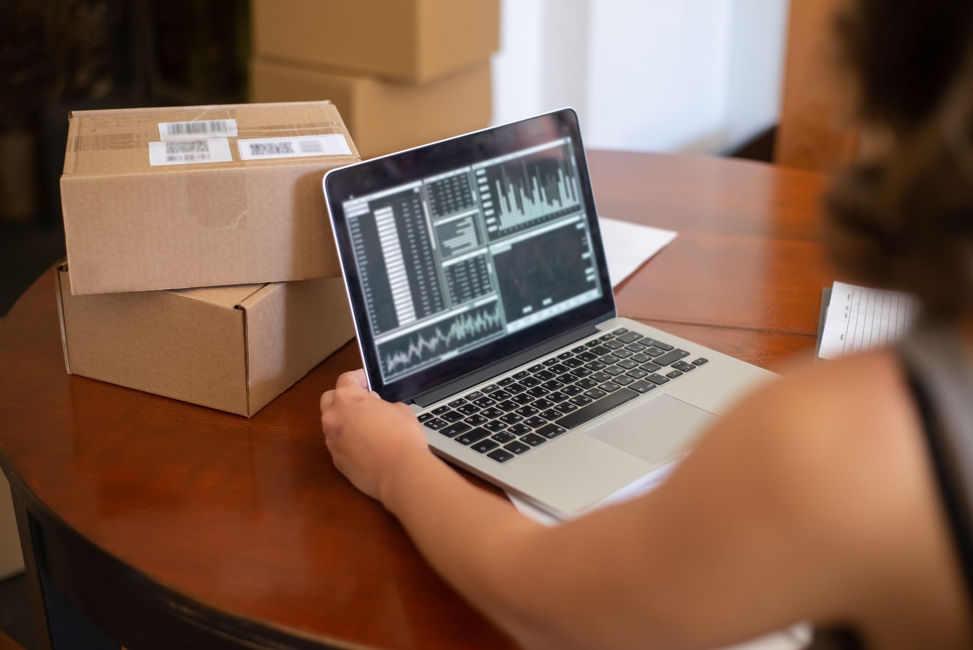 Person reviewing analytics dashboard on laptop beside parcels for online store security monitoring