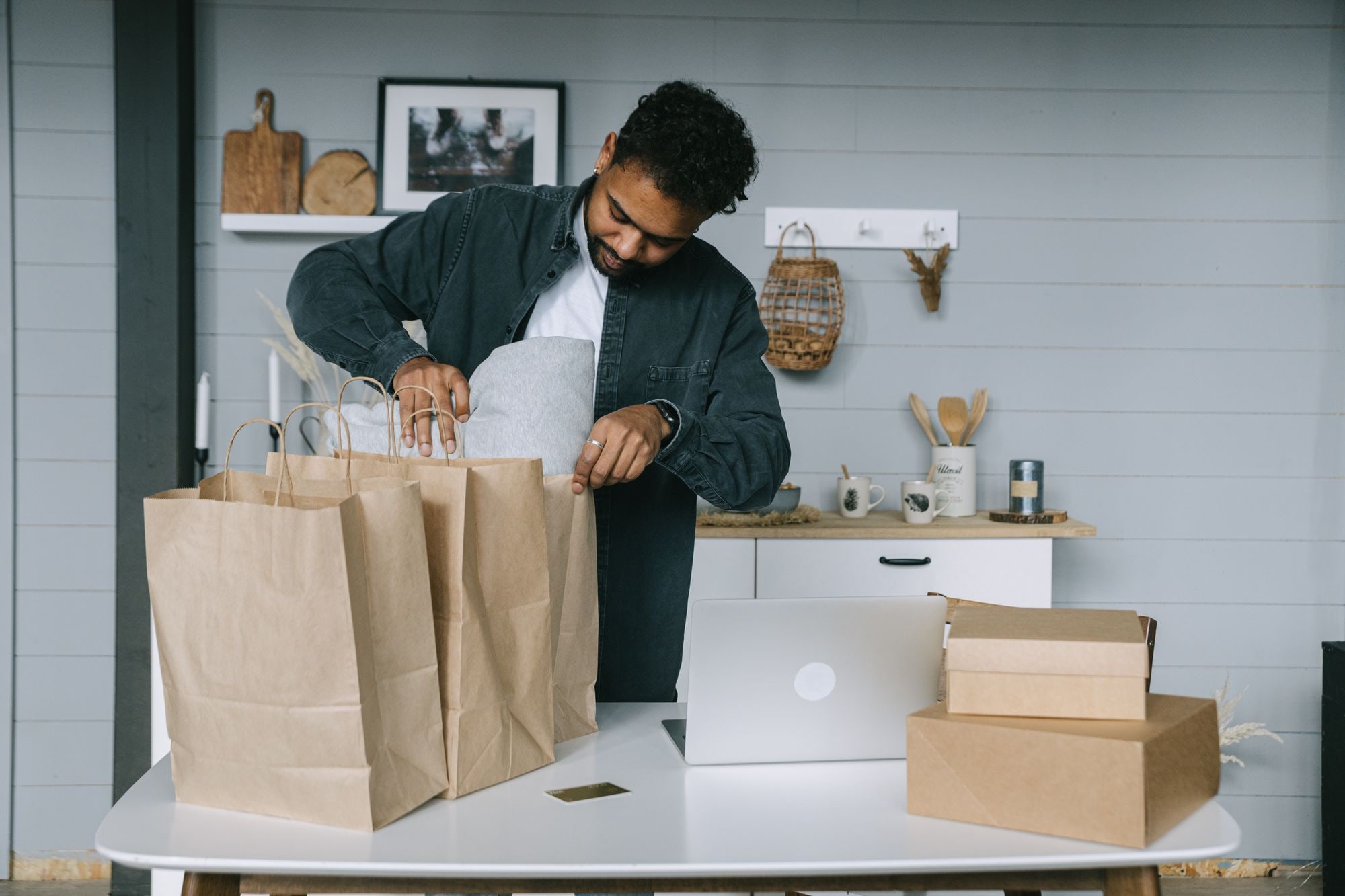 Small business owner packing orders into paper bags beside a laptop and shipping boxes for an online store